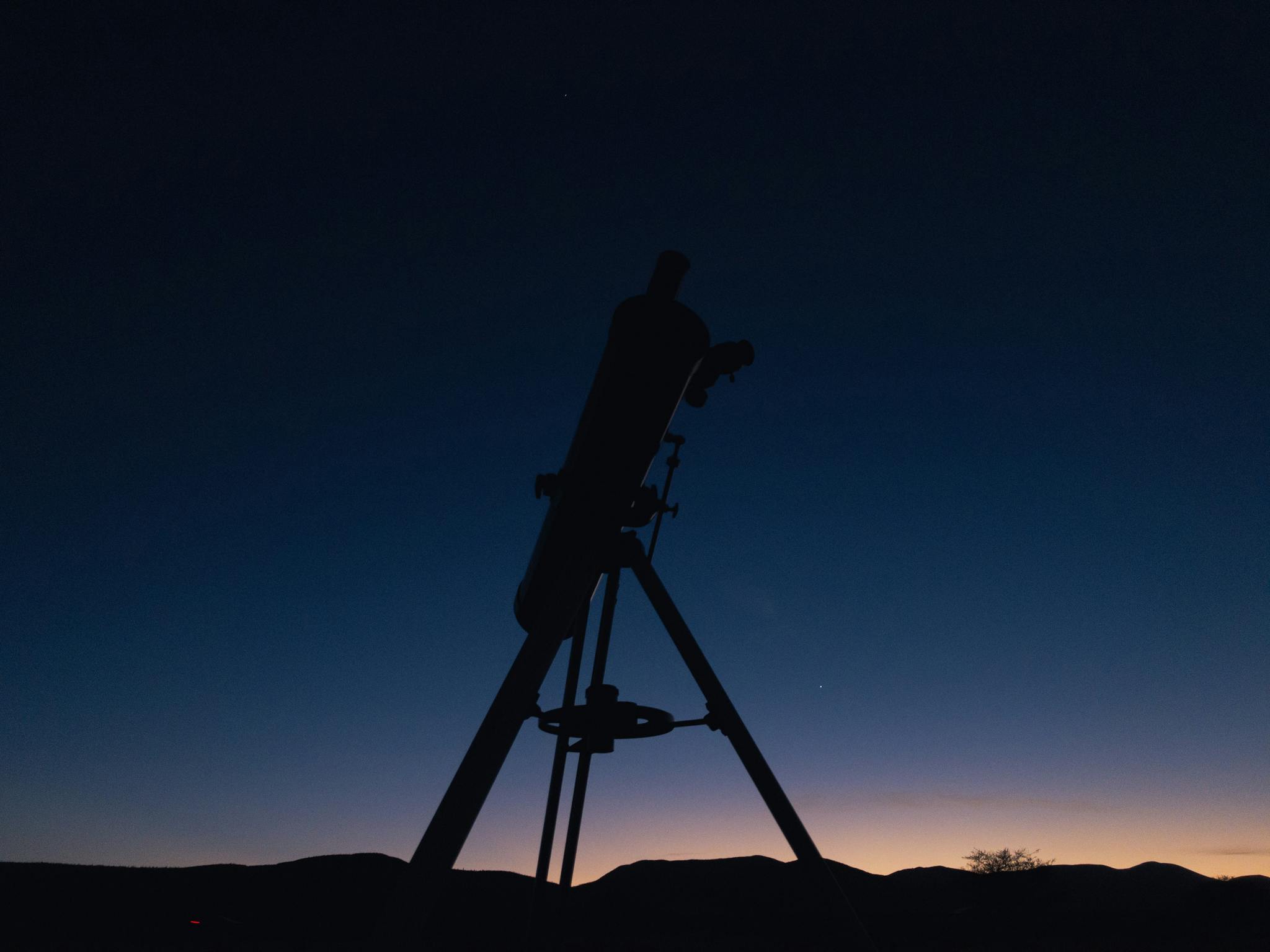 Silhouette of a telescope against a twilight sky, perfect for astronomy enthusiasts.